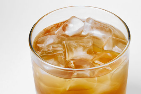 glass with a drink of dark color with ice, on a white background, alcohol