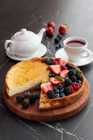 Pie with berries with a cut piece, with a cup of tea and teapot, strawberries, blackberries, blueberriesの写真素材