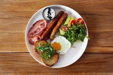 Breakfast with fried sausages, egg, ham, sausages and avocado and tomato saladの写真素材