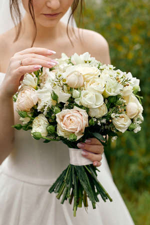 The bride in a wedding dress with open shoulders holds a bouquet of rosesの写真素材