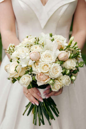 The bride in a wedding dress with open shoulders holds a bouquet of rosesの写真素材