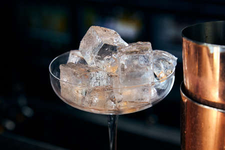 Large glass filled with ice cubes next to the shakerの写真素材