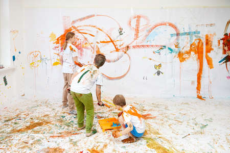 three children paint on a white wall with paints, boys and girlsの写真素材