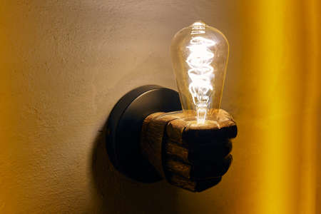 Hand shaped chandelier with glowing lightbulb on yellow wallの写真素材