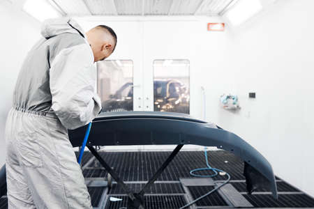 Worker in protective workwear applies paint on car bumperの写真素材