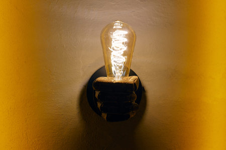 Fist shaped luster with glowing light bulb on yellow wallの写真素材