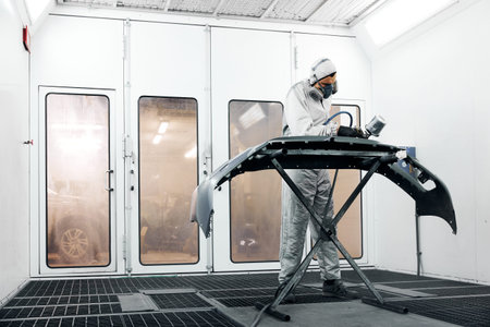 Employee in protective clothes with mask paints car bumperの写真素材