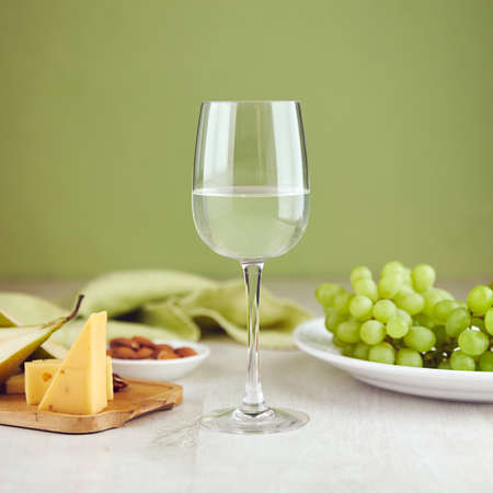 Glass of white wine with cheese and grape on table closeupの写真素材