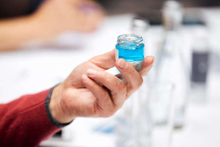 Man hand holds small jar with light blue liquid over tableの写真素材