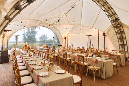 Served tables in tent prepared for wedding day on rainy dayの写真素材