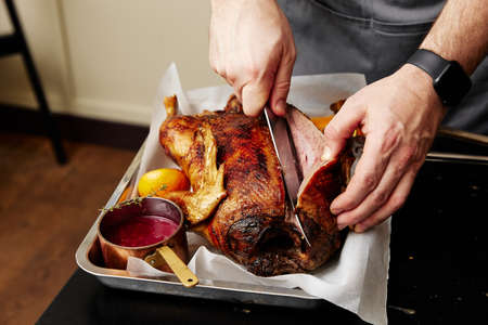Man cuts duck baked with orange fruits at table closeupの写真素材
