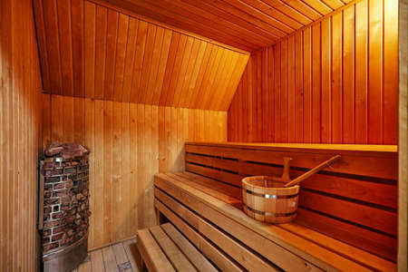 Wooden orange walls and benches in modern sauna with electric heater. Bathhouse cabin interior illuminated with light and sauna accessoriesの写真素材