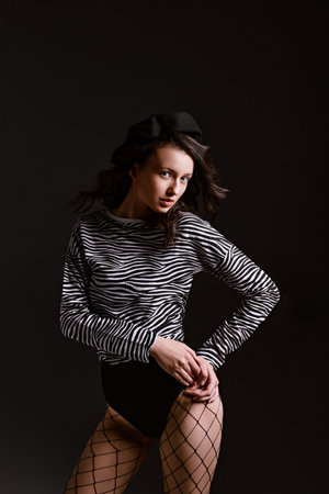 Professional model in jumper with zebra pattern poses for photo looking in camera. Brunette woman stands on dark background in studioの写真素材