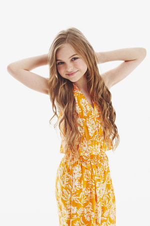 Sweet teen girl with long loose hair enjoys posing for photo in studio. Professional model in stylish orange outfit smiles standing on white backgroundの写真素材