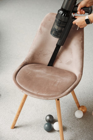 Person cleans chair from dust and litter with handheld wireless vacuum cleaner and takes care of furniture. Woman uses modern technology to clean houseの写真素材