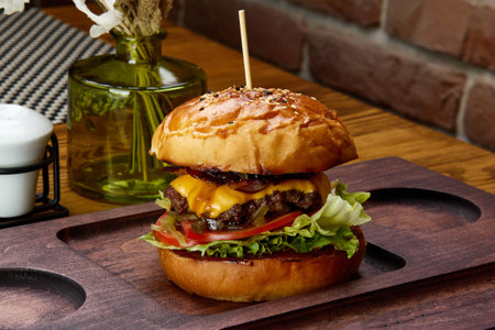 Large burger with cheese and cutlets served on wooden board attracts people. Tasty food attracts tourists to visit fast food cafe at resortの写真素材