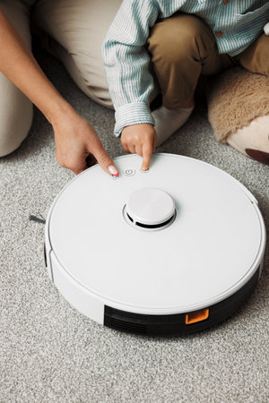 Parent and son examine together new purchase at home. People press buttons on new robot vacuum cleaner helping get rid of litter on floorの写真素材