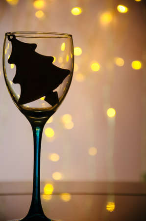 Silhouette of tree toy in the wineglass. Christmas background with lightsの写真素材