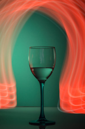 Wineglass on green background with red neon light painting behindの写真素材