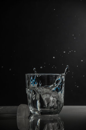 A piece of ice falls into a glass. Splashing out of itの写真素材