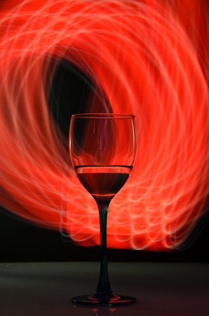 Wineglass on gray background with red neon light painting behindの写真素材