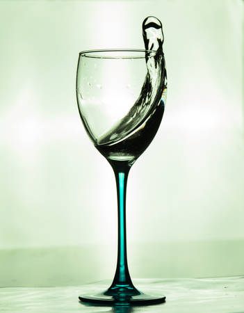 Wineglass with a splash of water on green backgroundの写真素材