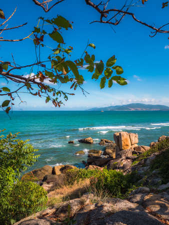 Rocks on the beach with island behind. Touristic place for vacation. Ocean with waves and moody skyの写真素材