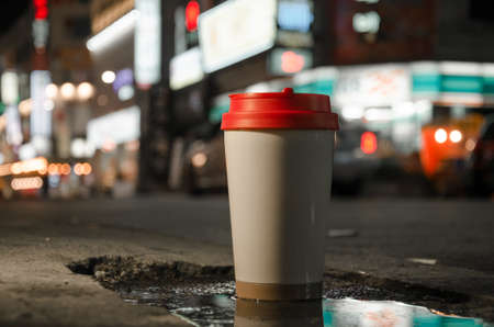 A glass of coffee is standing on the sidewalk. Street lights bokeh backgroundの写真素材