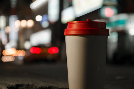 A glass of coffee is standing on the sidewalk. Street lights bokeh backgroundの写真素材