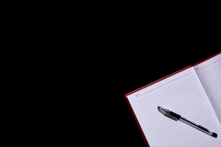 The diary with blank pages in the corner of the frame and a pen on top, a black isolated background,...