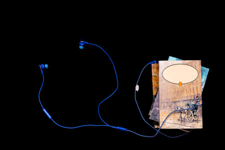 Audio books and modern technology concept - stack of art books entwined with blue headphones,...
