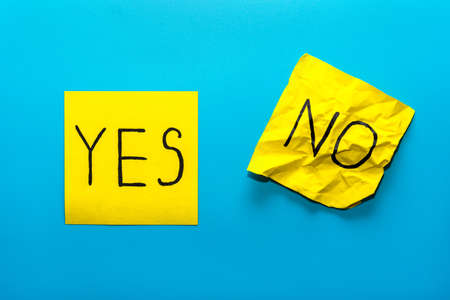 Close up black handwritten inscription yes and no word on two yellow square stickers on blue background with copy spase, horizontal orientationの写真素材