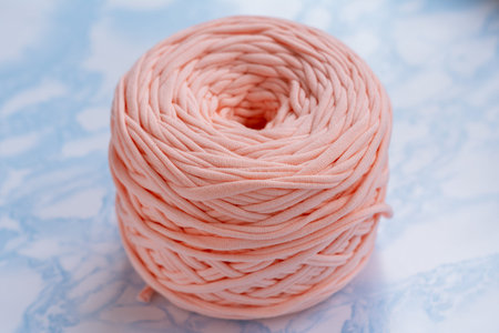 A coil of large knitted yarn of peach color on the surface of blue marble