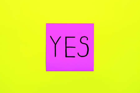 Close up black handwritten inscription yes word on one purple square sticker on yellow background with copy spase, horizontal orientationの写真素材