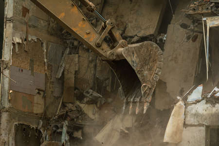Demolition of a five-story apartment building recognized as emergency housing, close-up of an excavator bucket collects construction wasteの写真素材