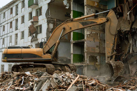 Demolition of a five-story apartment building recognized as emergency housing, close-up of an excavator bucket collects construction wasteの写真素材