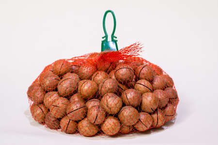 Macadamia nuts in a red mesh bag on a white backgroundの写真素材