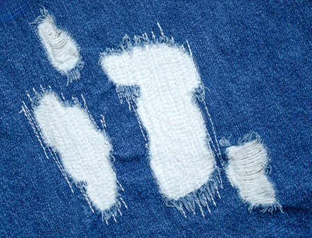 Close-up of blue denim jeans with visible white patch repair and frayed torn fabric for clothing restoration or fashion designの写真素材