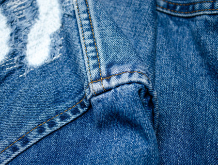 Close-up of blue denim jeans with visible white patch repair and frayed torn fabric for clothing restoration or fashion designの写真素材