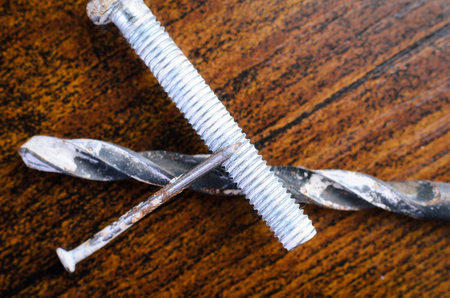 This image showcases a bolt, a nail, and a drill bit, all resting on a textured wooden background