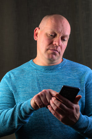 Man using smartphone, focused on screen, wearing a blue sweaterの写真素材