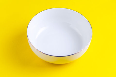 Elegant white bowl with gold trim on a vibrant yellow backgroundの写真素材