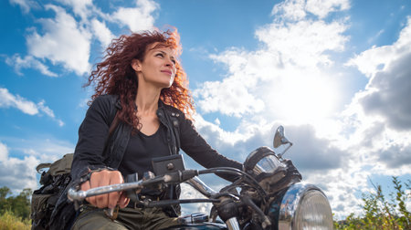Biker girl with red hair sitting on a motorcycle in the countrysideの素材