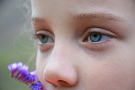 eyes of a girl close-up. turquoise eye color. near the cheeks, blurred silhouette of a wild flowerの写真素材