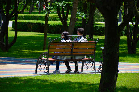 man and woman are sitting in a park on a bench. walk in the fresh air. rest while walkingの写真素材