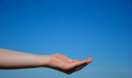 a woman's hand against the blue sky. the palm of the hand is folded, as if asking for somethingの写真素材