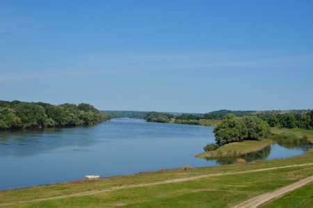 along the edges of the river, green banks, over the blue sky. on the right is a small island....