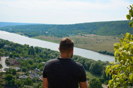 a young man on the edge of a cliff looks in front and admires the beautiful landscape