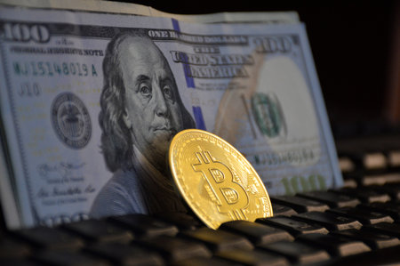a gold coin bitcoin on a computer keyboard is placed with an edge between the rows of letters on the...