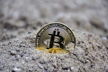 bitcoin gold coin half buried in sand symbolizes the search for treasure and the extraction of mineralsの写真素材